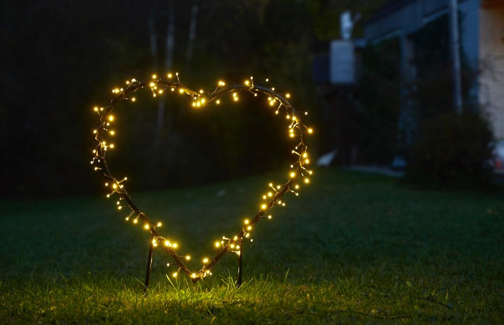 A heart-shaped light decoration with yellow LEDs is placed on a lawn at night.