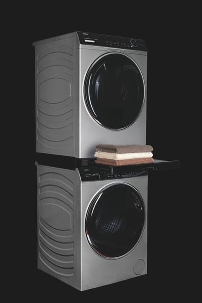 A stacked washing machine and dryer unit with a shelf and folded towels between them, set against a black background.
