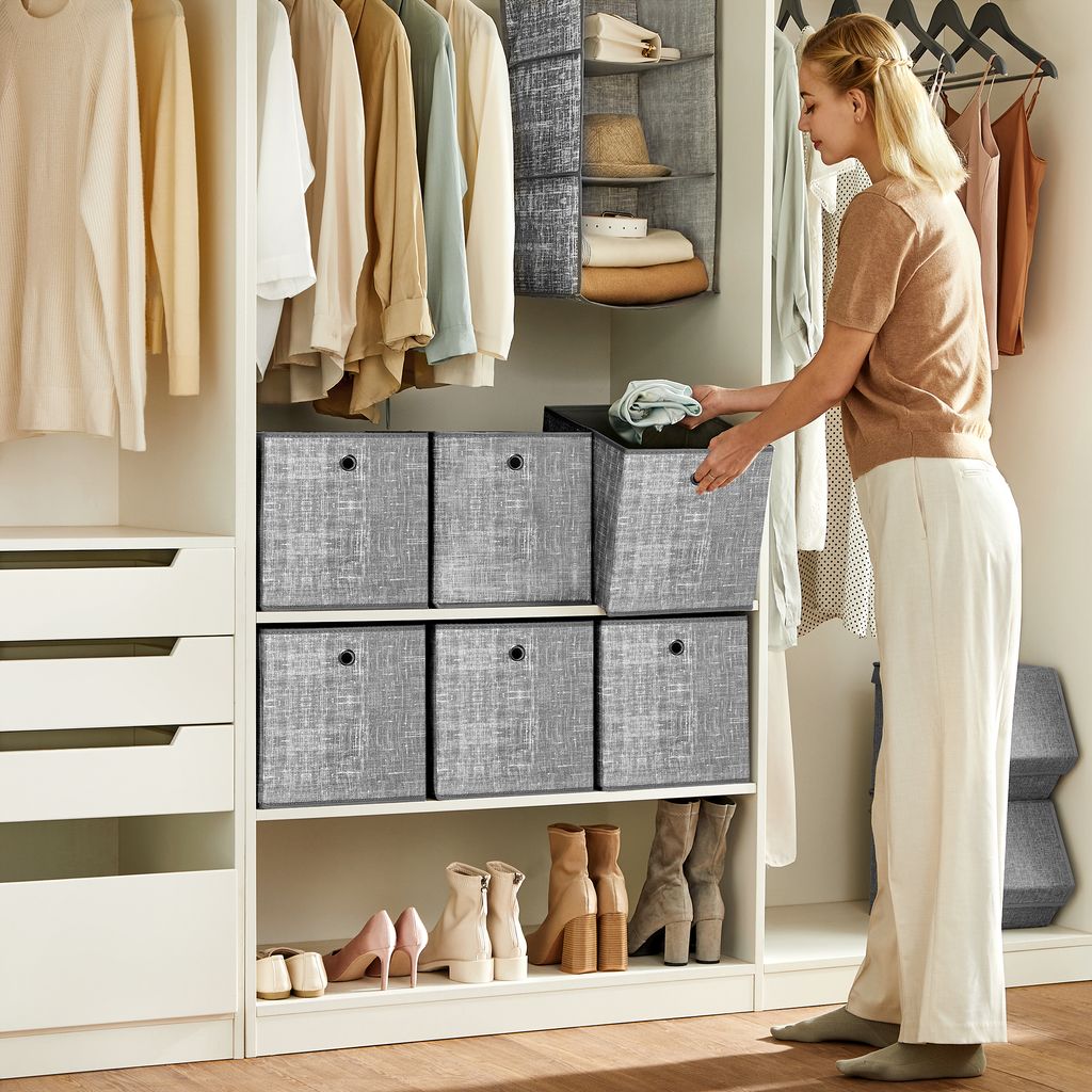 A woman is organizing items in a closet, placing a folded cloth into a storage box.