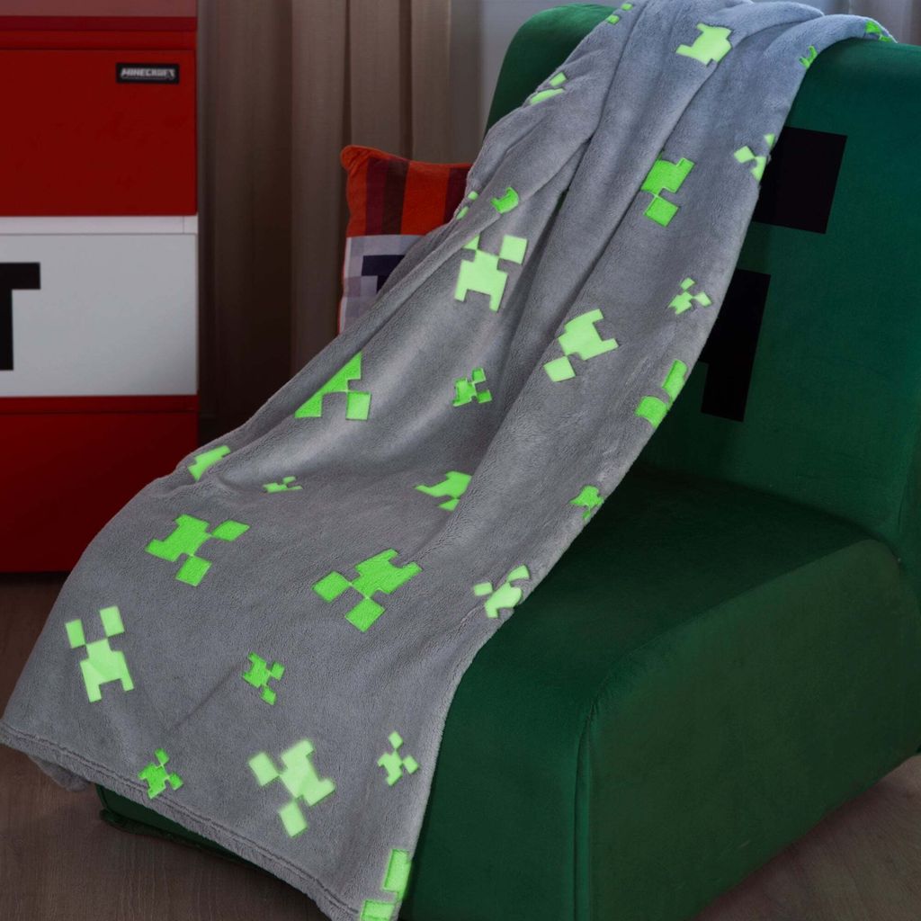 A Minecraft-themed blanket draped over a green chair, with a red and white TNT-like storage unit in the background.