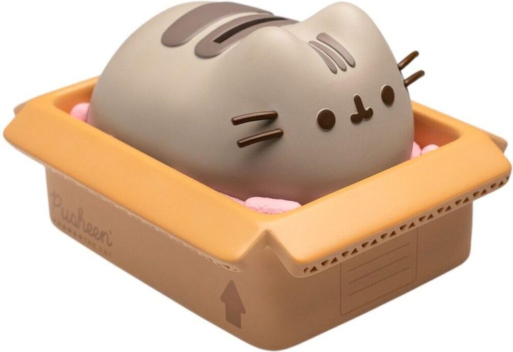 A Pusheen the cat figurine is sitting in a cardboard box filled with pink packing peanuts.