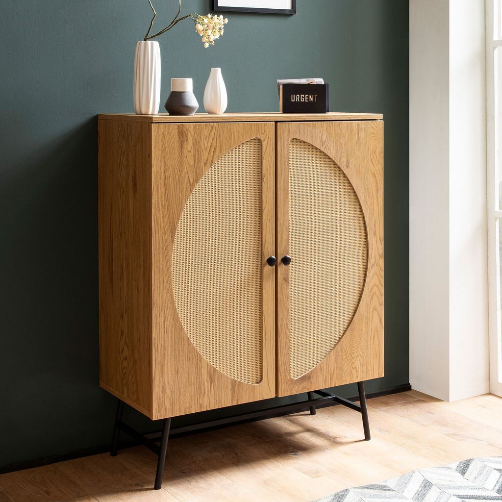 A wooden sideboard with rattan woven doors stands against a dark green wall, with decorative items on top.