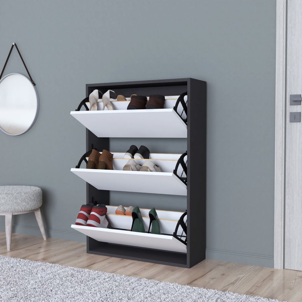 A dark gray shoe cabinet with three white flip-down compartments, each containing shoes, is shown against a light gray wall. A circular mirror hangs on the wall to the left, and a stool is partially visible in the foreground.