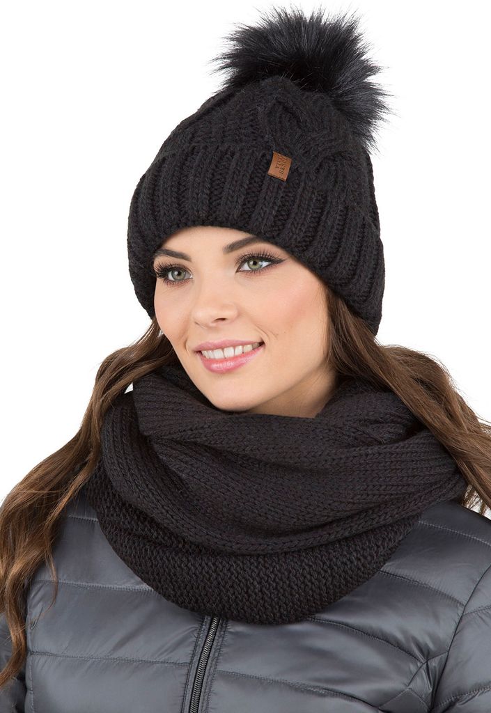 A woman wearing a black knitted hat with a pom-pom and a matching infinity scarf.