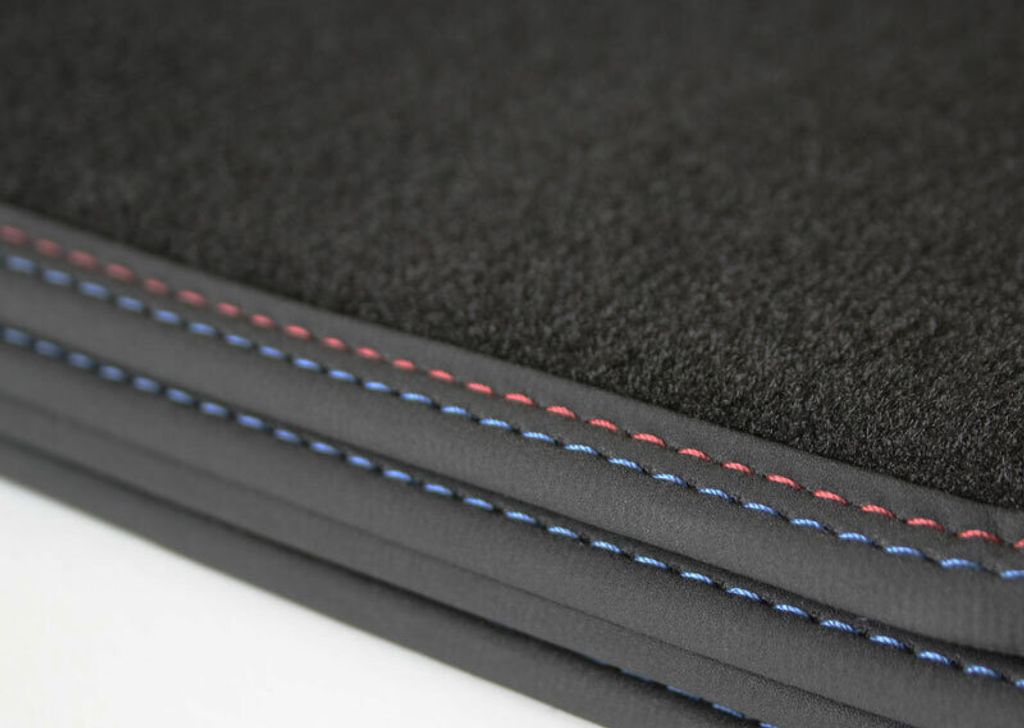 A close-up view of the edge of a car floor mat, showing the black carpet and stitched trim in red and blue.