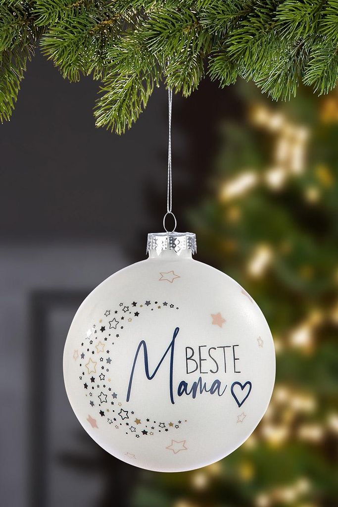 A white Christmas ornament with stars and the text 'Beste Mama' hangs from a pine branch.