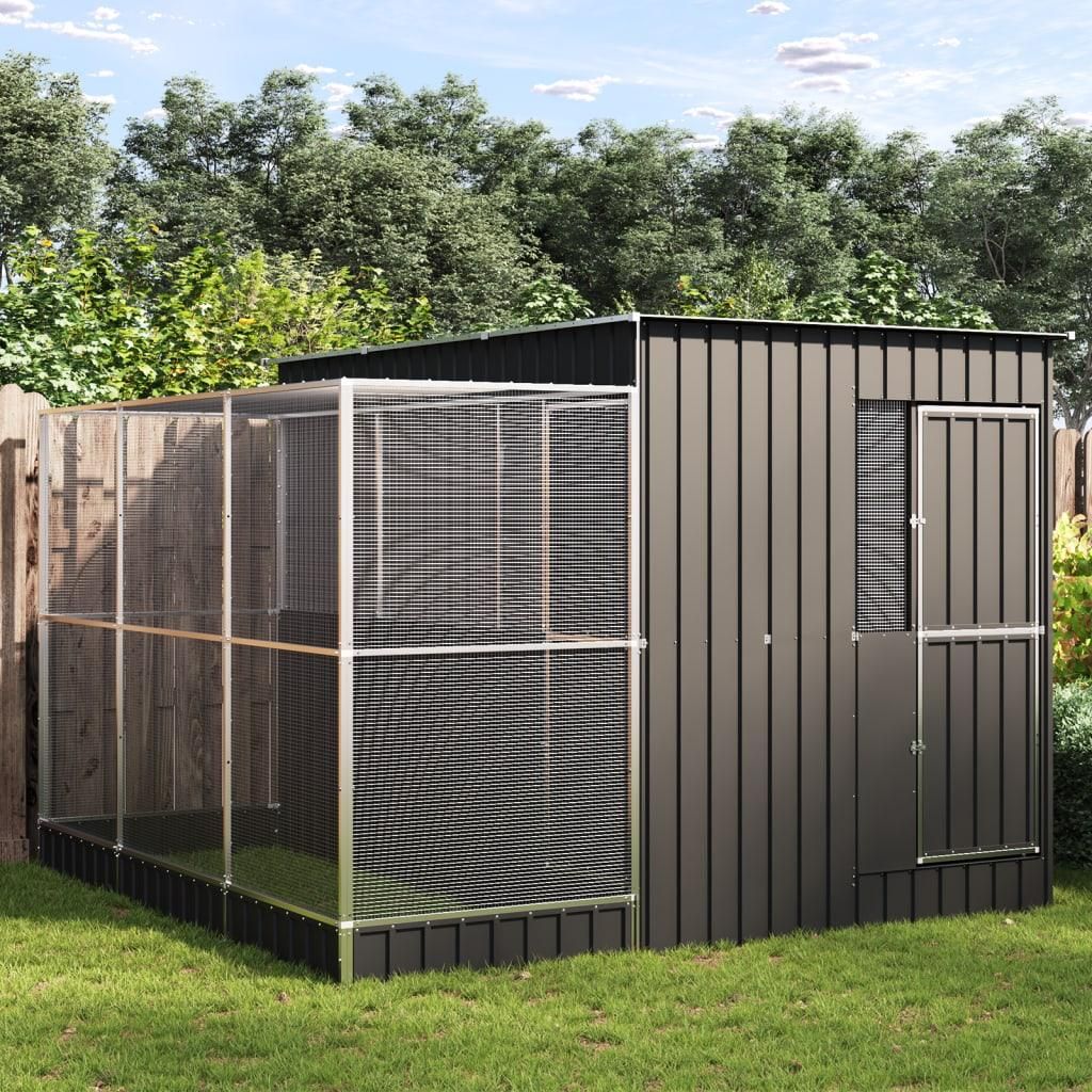 A metal and mesh aviary structure is set up in a grassy backyard with trees in the background.