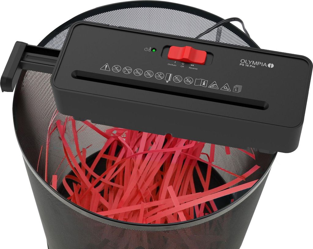 A black paper shredder is placed on top of a black trash bin, shredding red paper into strips.