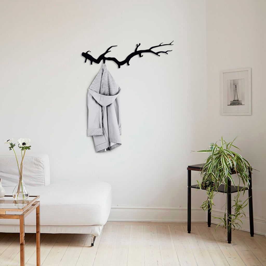 A coat rack shaped like a tree branch hangs on a white wall, with a coat draped over it. A sofa and a side table with a plant are also visible.