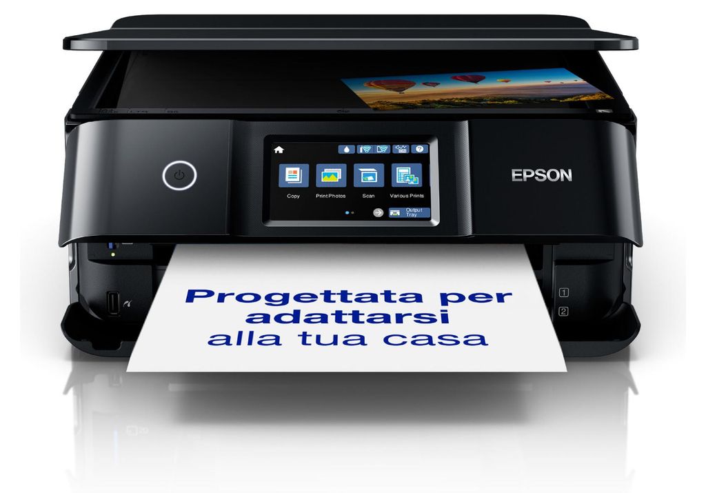 A black Epson printer is shown from the front, printing a sheet of paper with Italian text. The printer has a touchscreen display and a picture is visible in the scanner lid.