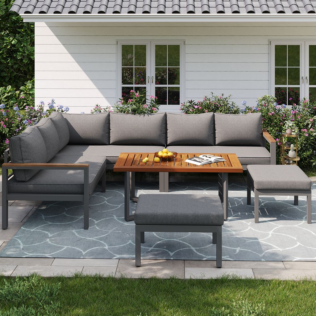 An outdoor patio set with a sectional sofa, coffee table, and ottomans on a patio with grass and flowers.