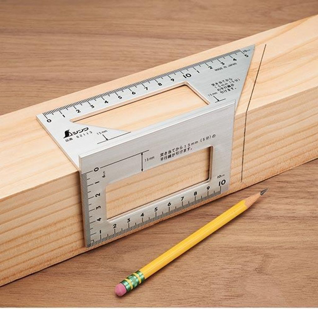 A metal combination square is placed on a wooden beam, with a pencil nearby, indicating its use in woodworking or construction.
