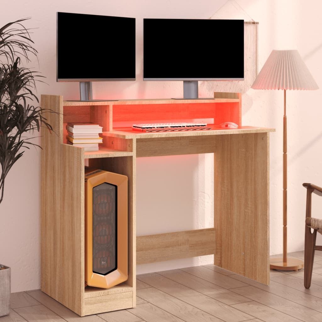 A modern computer desk with dual monitors, a keyboard, mouse, and a computer tower. The desk has built-in LED lighting.