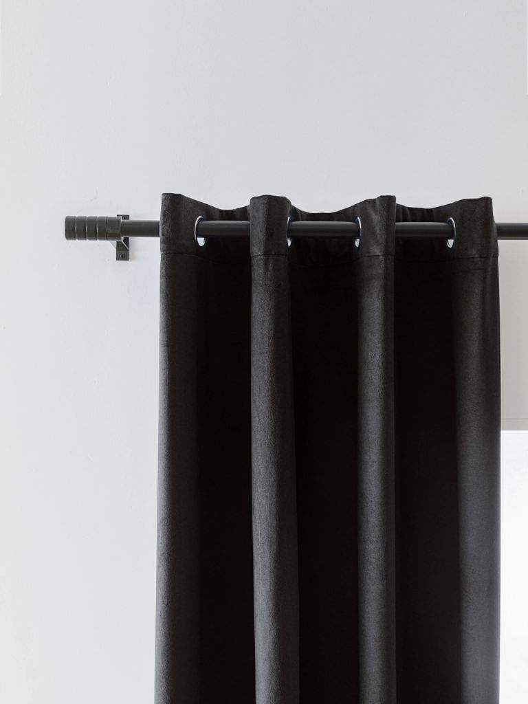 A close-up view of a black curtain hanging from a curtain rod against a white wall.