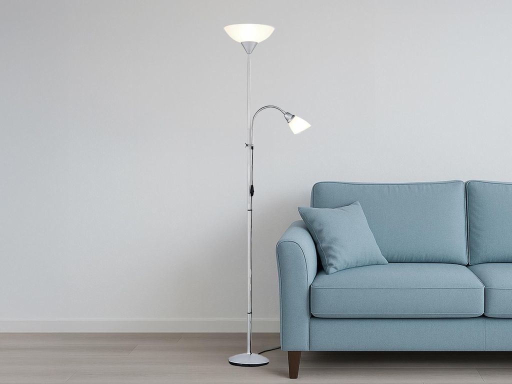 A silver floor lamp with two lights stands next to a light blue sofa against a white wall.