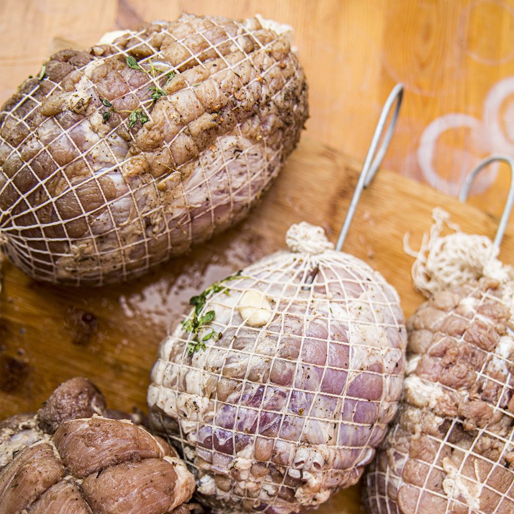 Several portions of meat wrapped in netting, seasoned and ready for cooking.