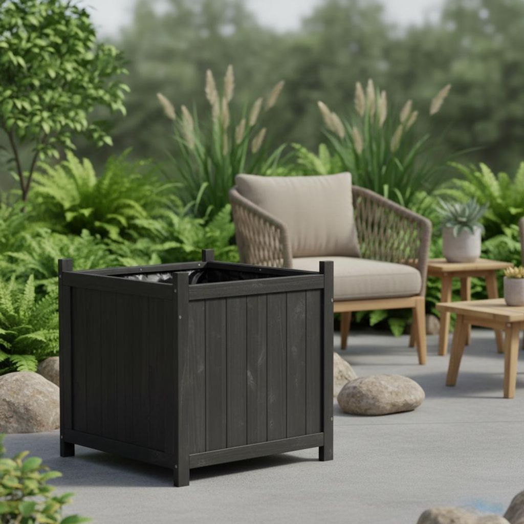 A dark gray wooden planter box sits on a patio, surrounded by rocks and lush green plants. A chair and small tables are visible in the background.