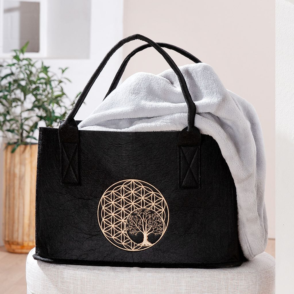 A black felt tote bag with a golden tree and flower of life motif, containing a light gray blanket.
