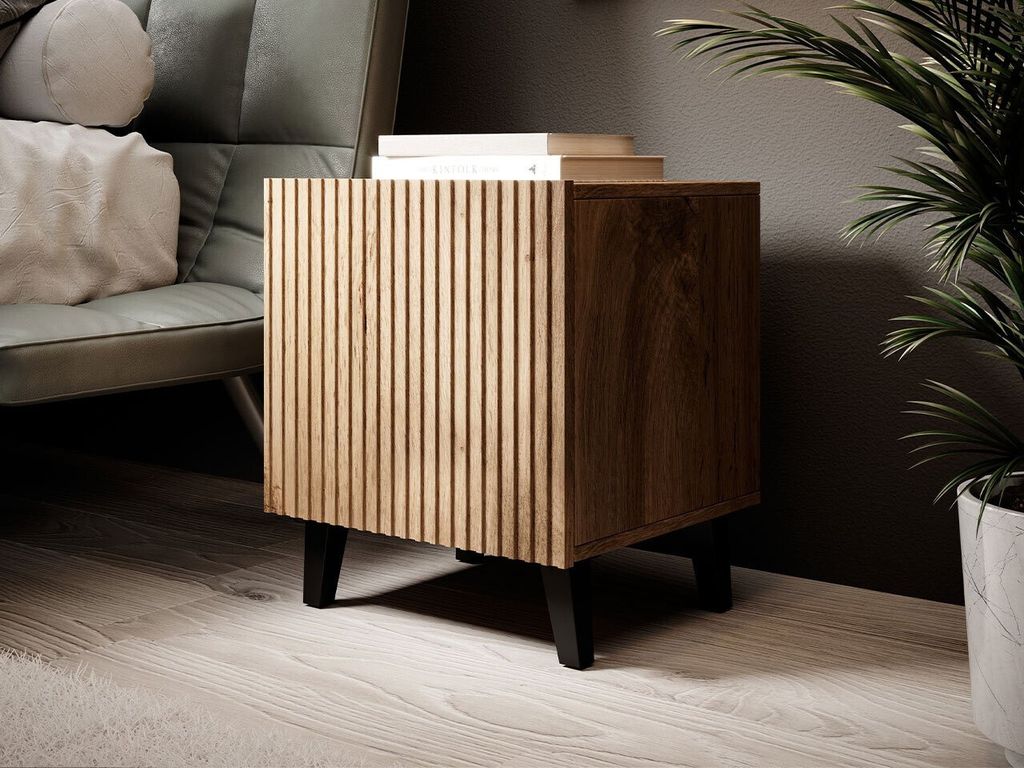 A wooden nightstand with a fluted front is placed next to a chair and a plant.