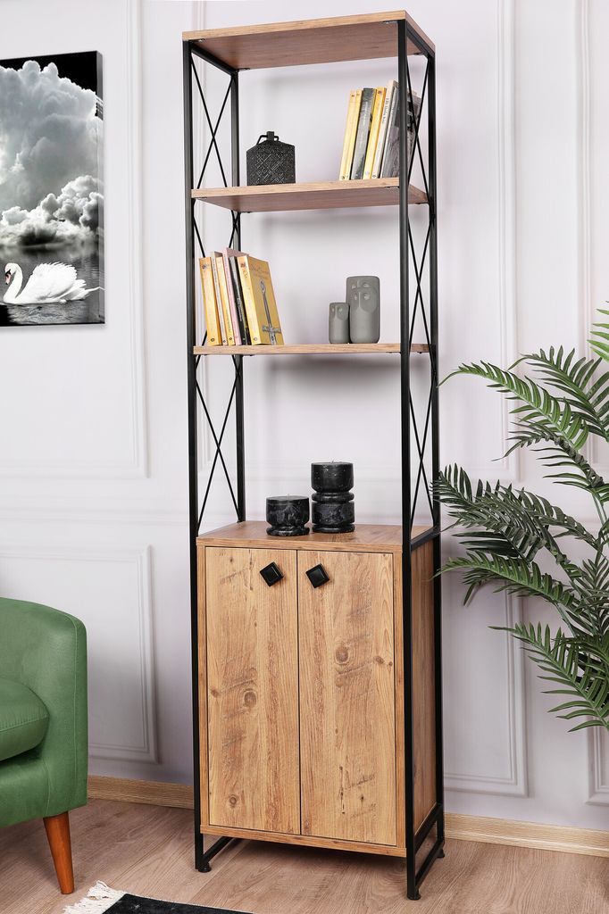 A tall, narrow bookshelf with a wooden cabinet at the bottom, set against a white wall with a green chair and a plant visible.
