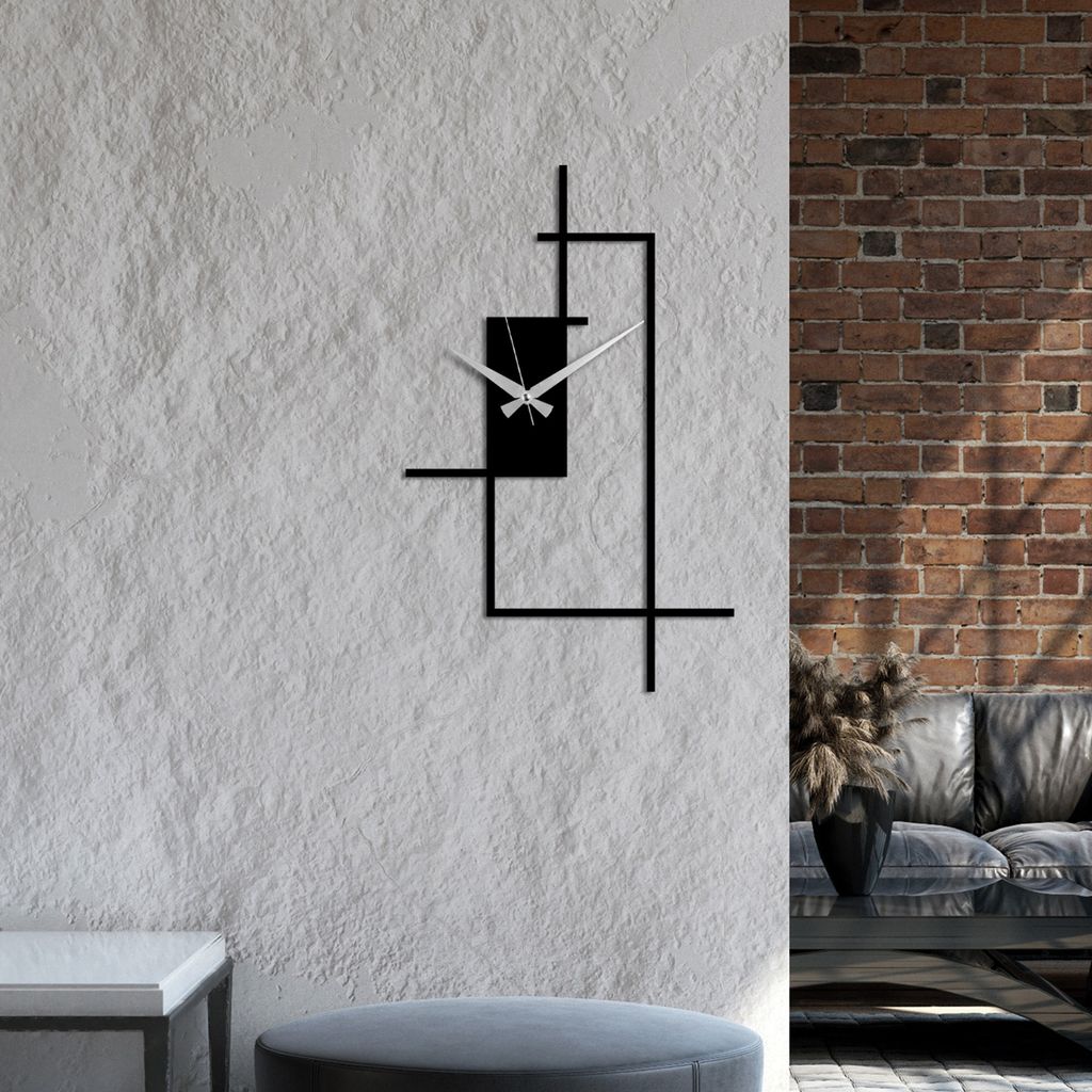 A modern black metal wall clock with a minimalist design is mounted on a textured white wall, with a brick wall and a sofa visible in the background.