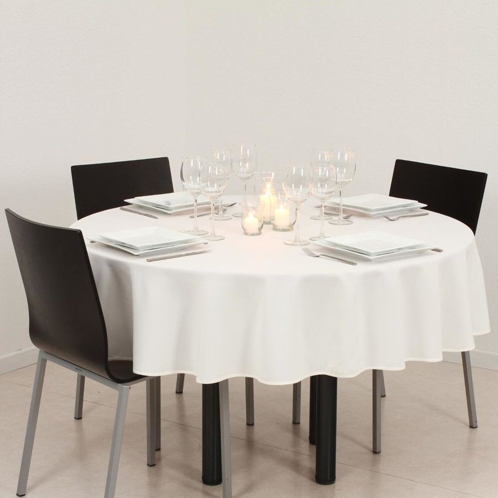 A round table set for a meal with white tablecloth, plates, glasses, and candles.