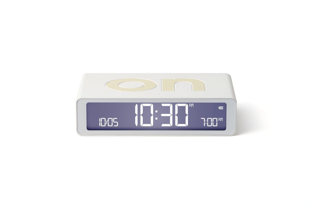 A white digital alarm clock with a gray display is shown against a white background.