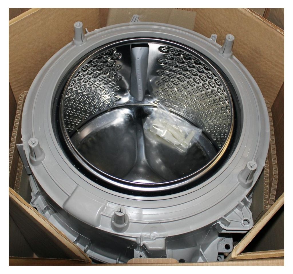 A washing machine drum and outer casing are shown inside a cardboard box.