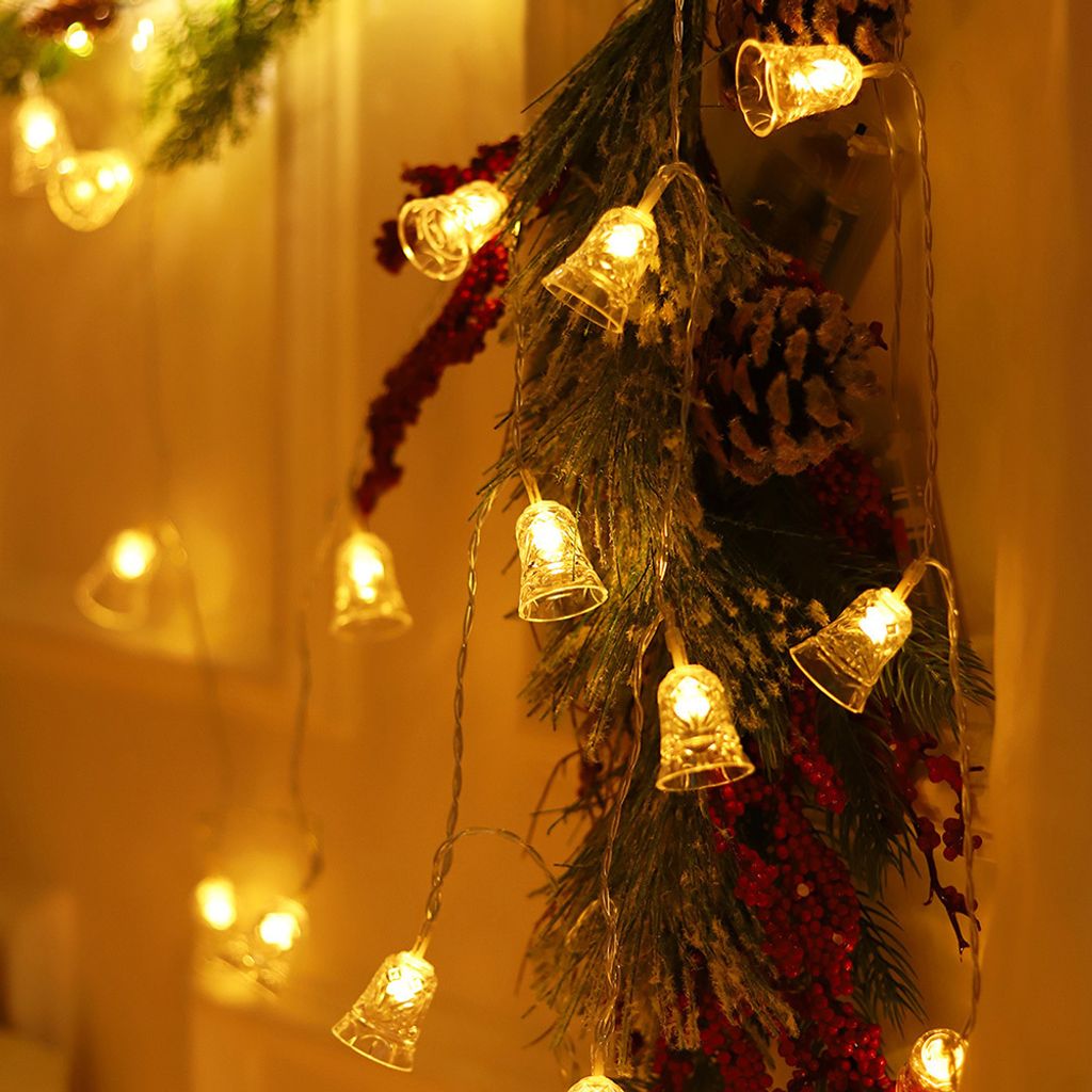 A close-up shot of a Christmas garland with bell-shaped lights, pine cones, and red berries.