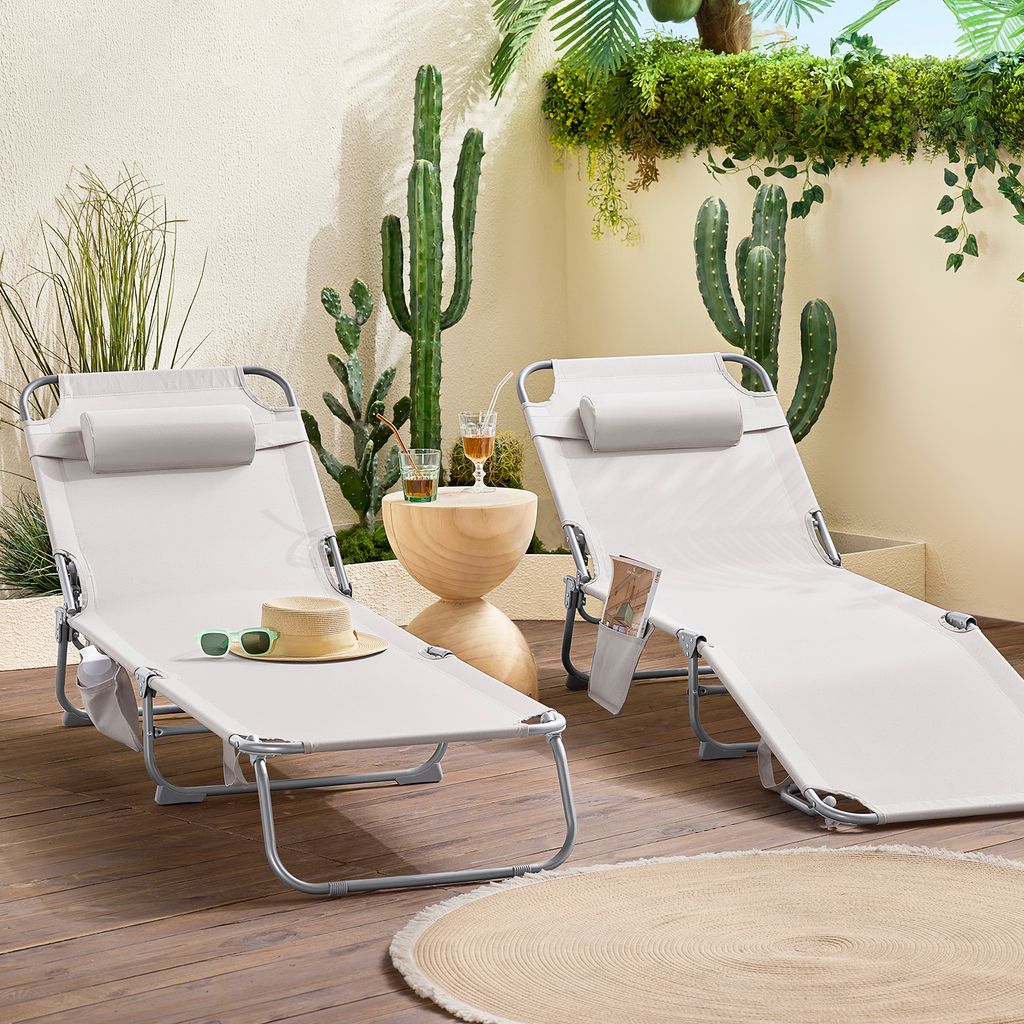 Two beige lounge chairs are set up on a wooden deck, surrounded by potted plants and cacti, creating a relaxed outdoor oasis.