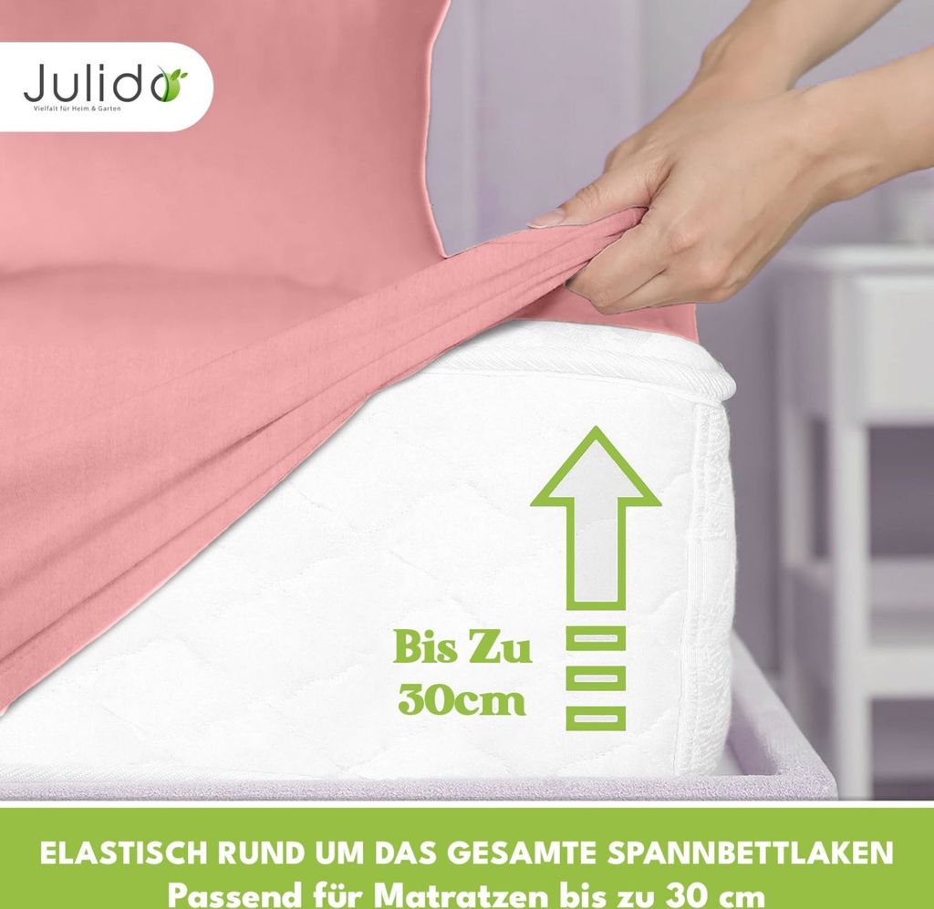 A hand is stretching a pink fitted sheet over a mattress.