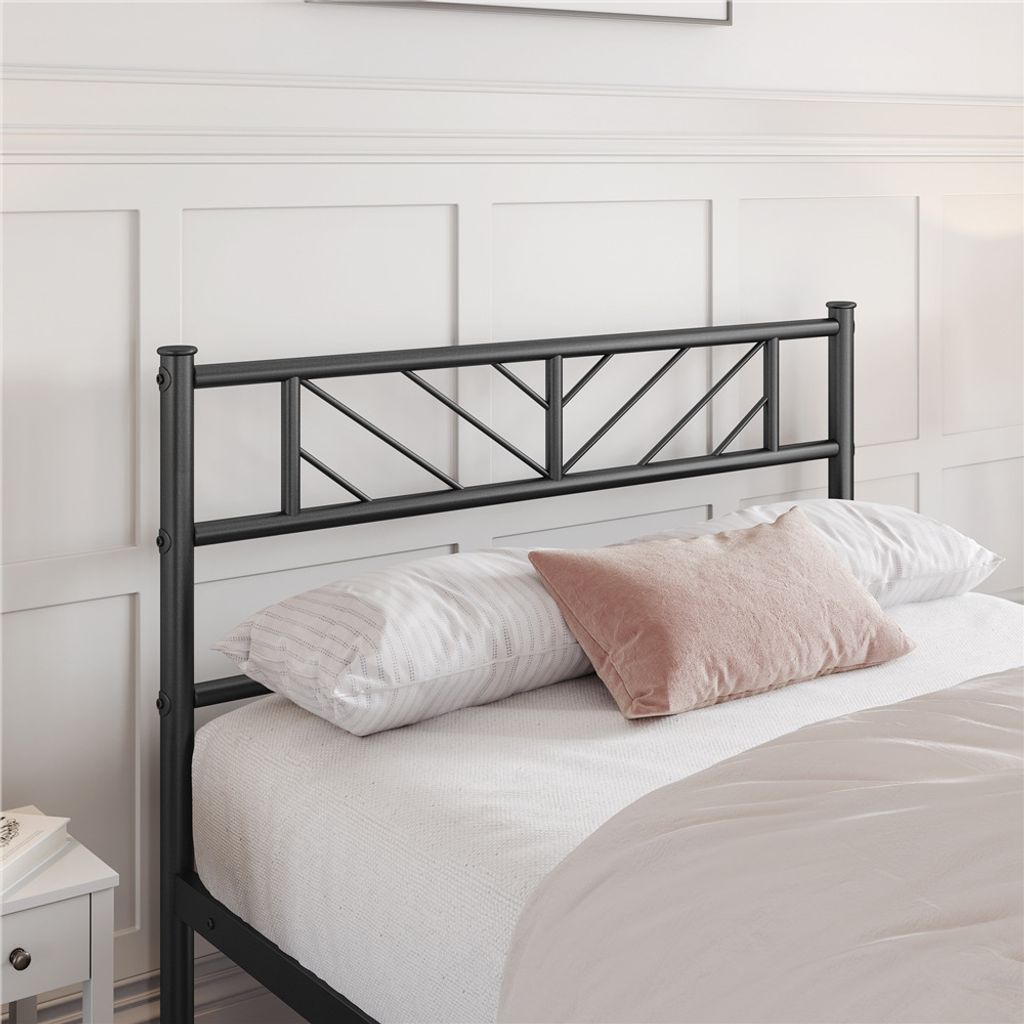 A close-up view of a black metal bed frame headboard with white bedding and a pink pillow.