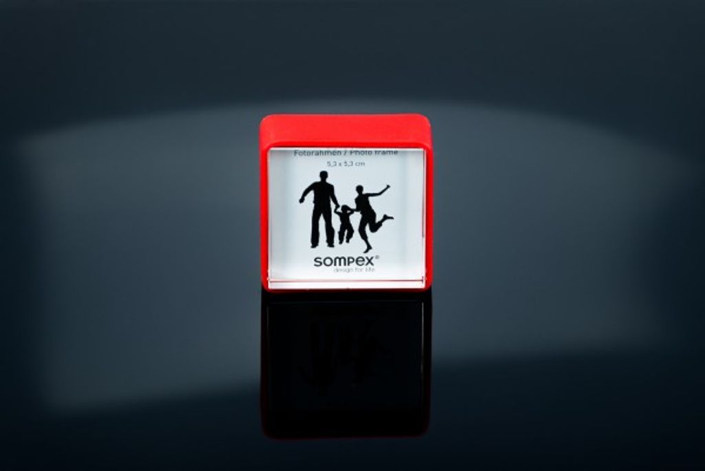 A small red photo frame with a silhouette of a family is displayed on a reflective black surface with a gradient gray background.