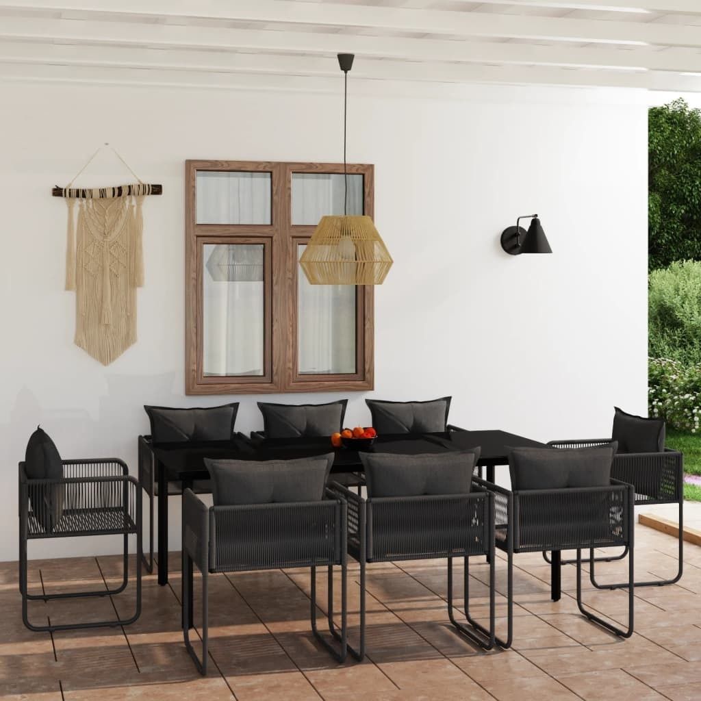 An outdoor dining set with chairs and a table on a patio, next to a wall with a window and macrame wall hanging.
