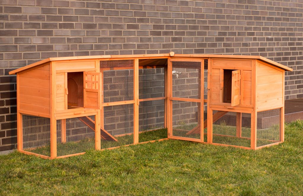 A wooden chicken coop with an attached run, set up on a grassy lawn in front of a brick wall.