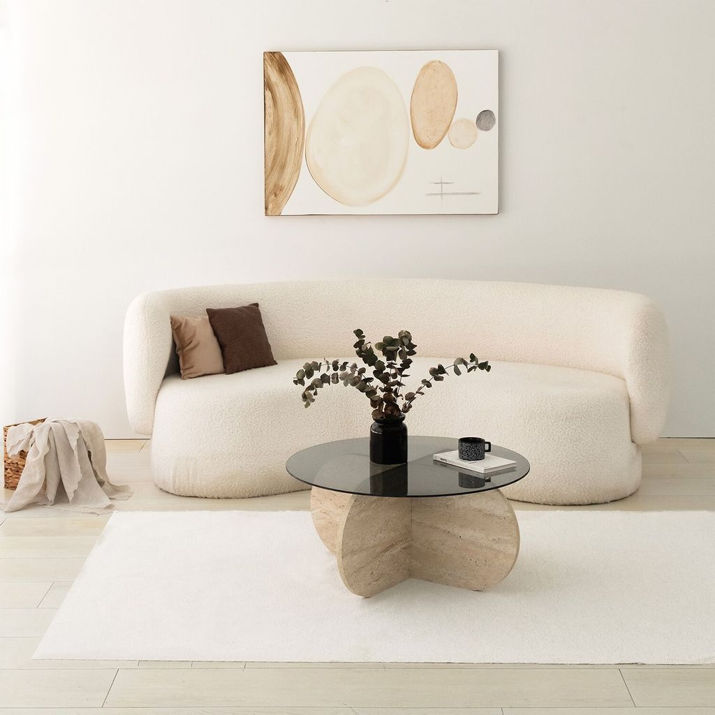 A modern living room scene with a fluffy white couch, a glass-top coffee table, and abstract art on the wall.