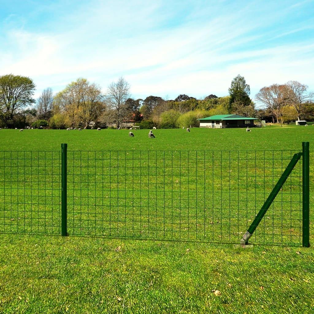 A green wire fence in a grassy field with sheep and a building in the background.