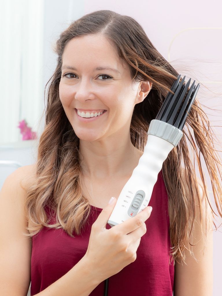 A woman is using a hair dryer with a comb attachment to dry her hair.