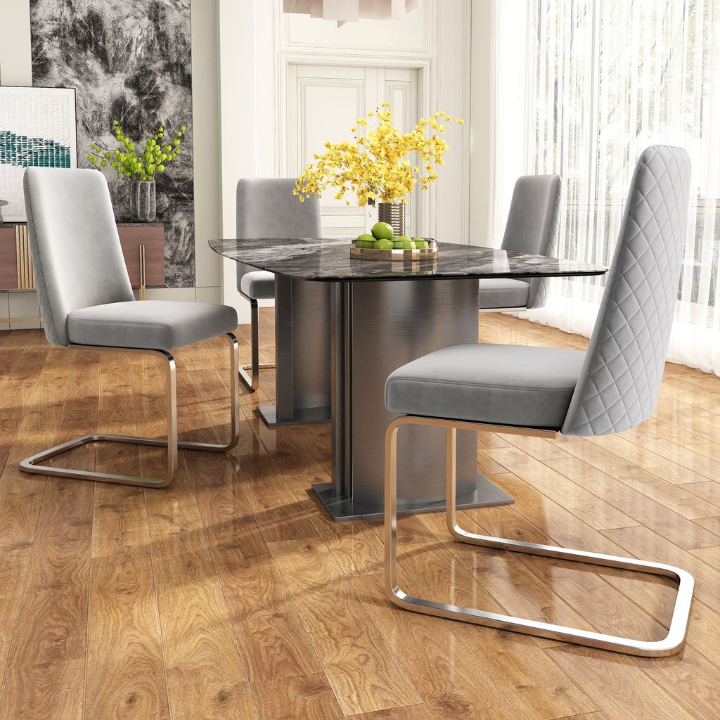 A dining room set with a marble-top table and four gray velvet chairs with silver metal legs.