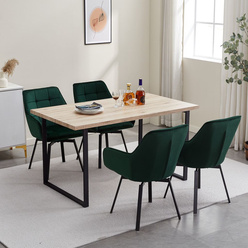 A dining set with four green velvet chairs around a light wood table in a well-lit room.