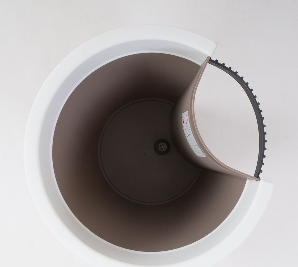 Top-down view of a planter with a white outer rim and a brown inner pot. A section of the inner pot is peeled back, revealing a black serrated edge.
