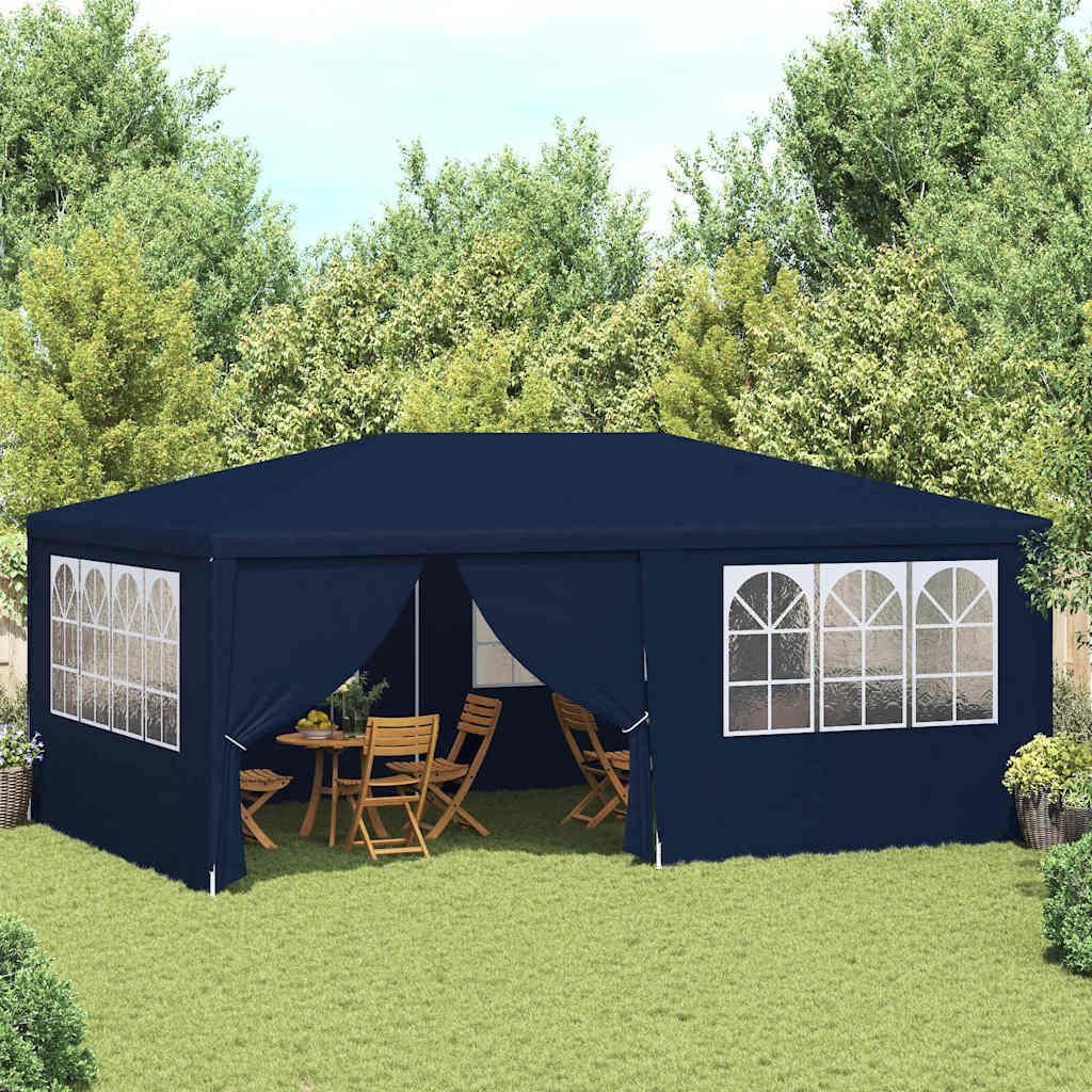 A navy blue party tent set up in a grassy backyard with trees in the background. A table and chairs are visible inside the tent.