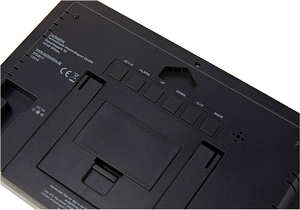 The back of a black digital clock, showing buttons and manufacturer information.
