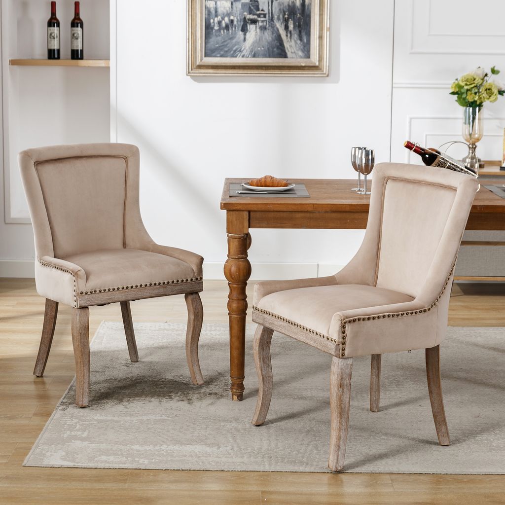 Two beige upholstered dining chairs are placed around a wooden dining table in a well-lit room.