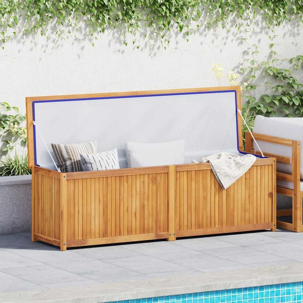 A wooden storage box with cushions and a blanket inside, placed on a patio next to a swimming pool, with greenery in the background.