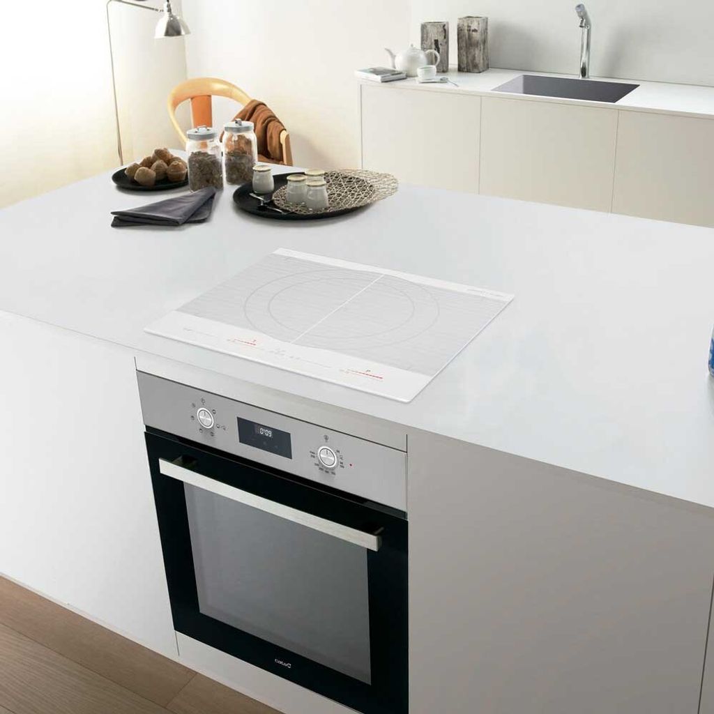 A modern kitchen island with a white countertop, featuring a built-in oven and an induction cooktop.