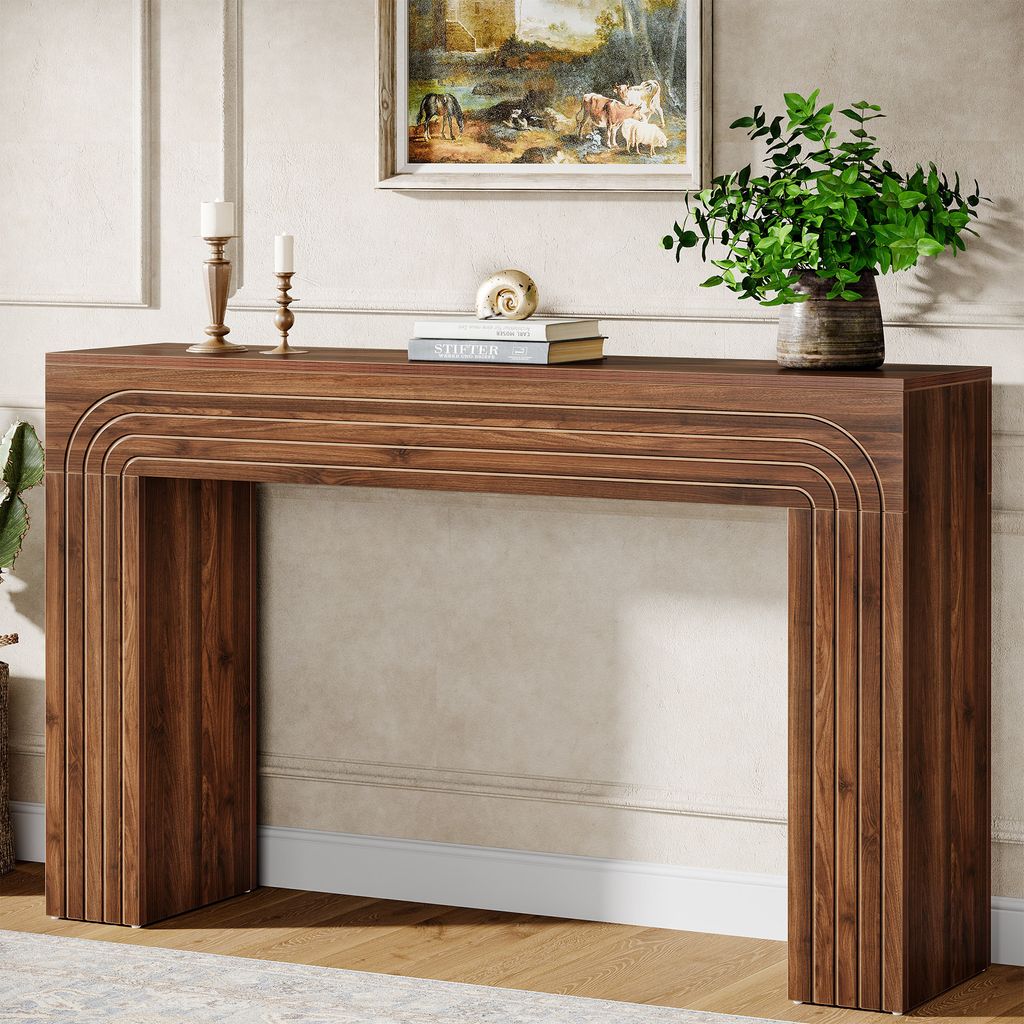 A wooden console table with decorative carvings is placed in a well-lit room, adorned with candles, books, and a potted plant.