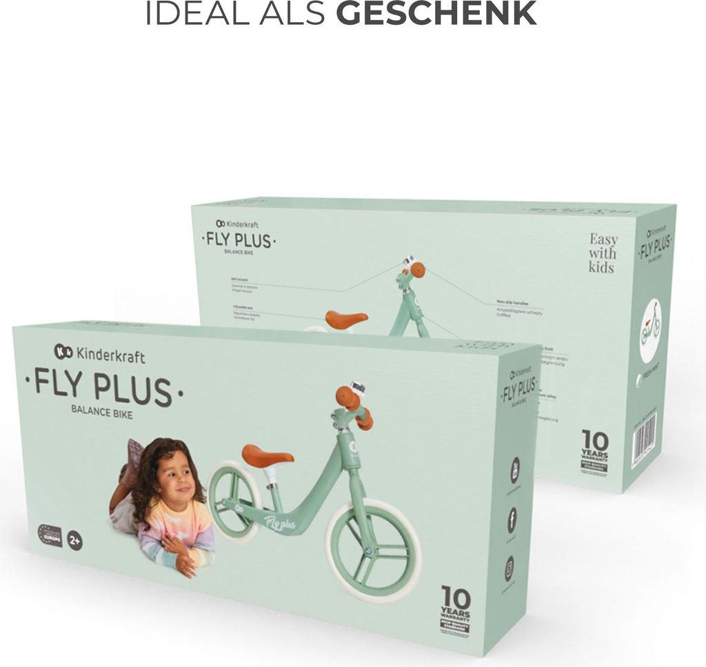 Two boxes of Kinderkraft FLY PLUS balance bikes are shown, one in the foreground and one in the background. A child is lying next to the foreground box.