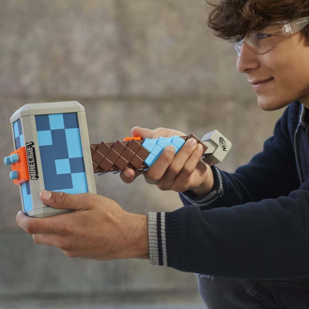 A young person wearing safety glasses is holding a Minecraft-themed Nerf hammer.