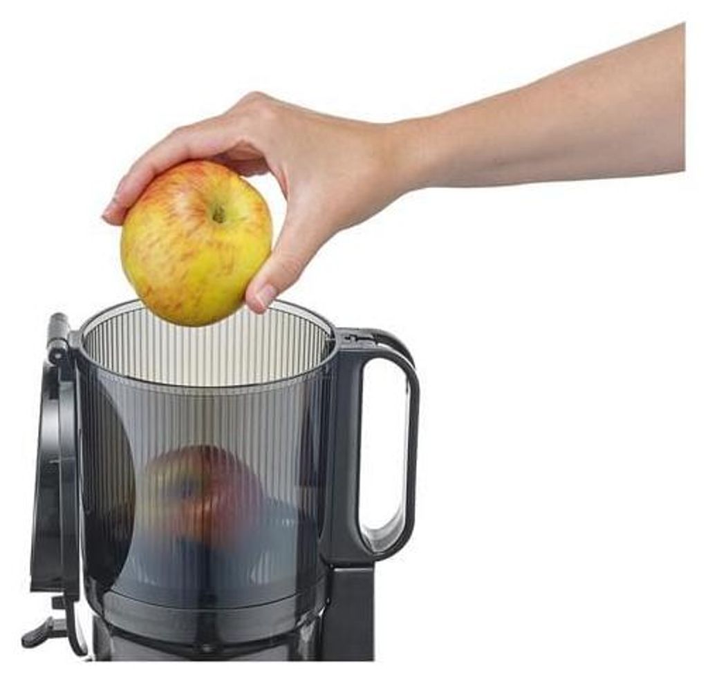 A hand is shown placing an apple into a juicer.